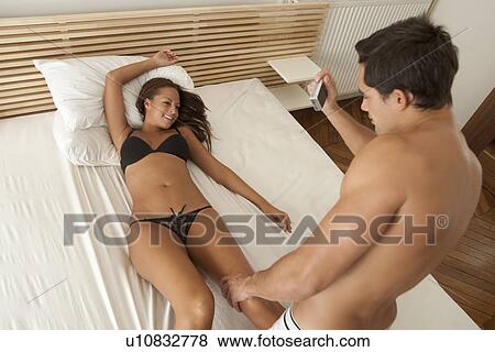 Stock Photo - Man taking pictures of girlfriend in bed. Fotosearch