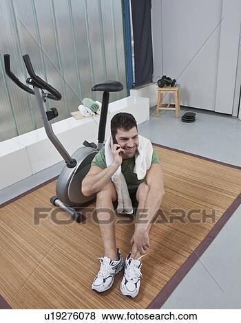 Stock Photo - Man talking on cell phone in home gym. Fotosearch