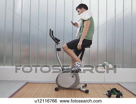 Stock Photograph - Man using cell phone on exercise machine. Fotosearch