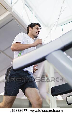 Stock Photo - Man using exercise machine in gym. Fotosearch