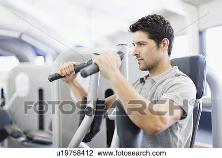 Stock Image - Man using weights machine in gym. Fotosearch