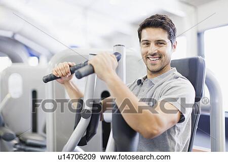 Stock Photo - Man using weights machine in gym. Fotosearch
