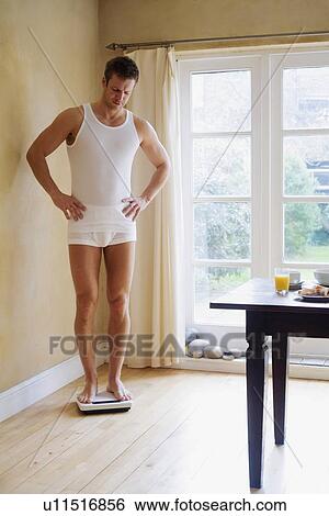 Stock Photograph - Man weighing himself in kitchen. Fotosearch