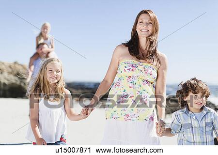 Stock Image - Mother and children walking on beach. Fotosearch