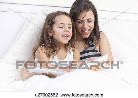 Stock Image - Mother and daughter reading in bed. Fotosearch