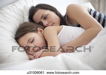 Stock Image - Mother and daughter relaxing in bed. Fotosearch