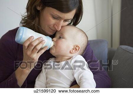 Stock Image - Mother bottle feeding baby on sofa. Fotosearch
