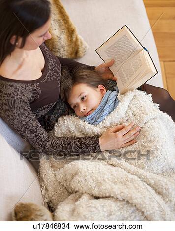 Mother reading to daughter on sofa View Large Photo Image Picture - Mother reading to daughter on sofa. Fotosearch