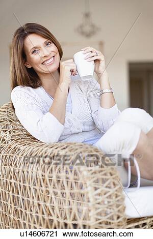 Stock Image - Older woman having coffee in armchair. Fotosearch