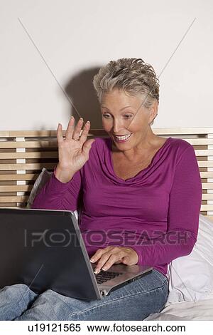 Older woman using laptop on bed View Large Photo Image Stock Photography - Older woman using laptop on bed. Fotosearch