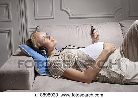 Stock Image - Pregnant woman listening to headphones. Fotosearch
