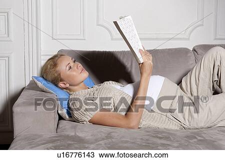 Stock Image - Pregnant woman reading on sofa. Fotosearch