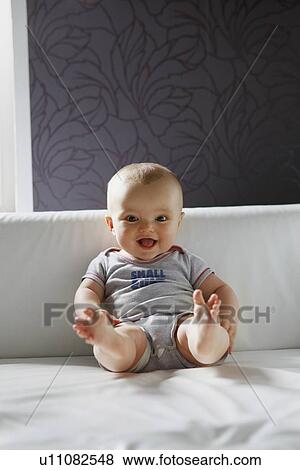 Stock Photo - Smiling baby sitting on sofa. Fotosearch