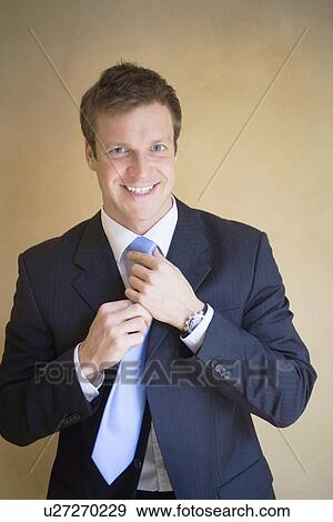 Stock Photo - Smiling businessman adjusting his tie. Fotosearch