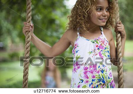 Picture - Smiling girl standing on tree swing. Fotosearch