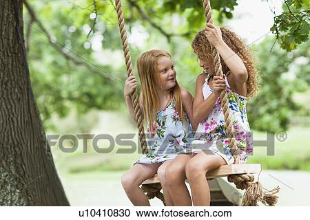 Stock Image - Smiling girls sitting in tree swing. Fotosearch