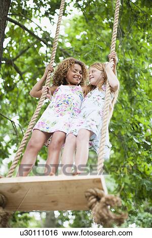 Smiling girls standing on tree swing View Large Photo Image Stock Photograph - Smiling girls standing on tree swing. Fotosearch