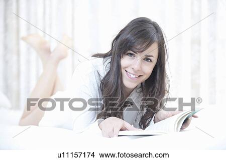 Picture - Smiling woman reading in bed. Fotosearch