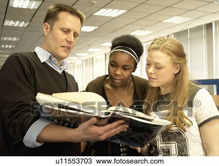 Stock Image - Students reading with teacher in library. Fotosearch