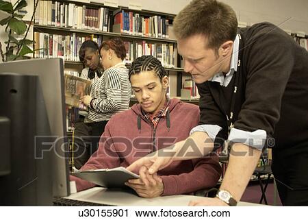 Stock Image - Teacher helping student in library. Fotosearch