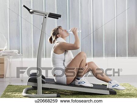 Woman drinking water on exercise machine View Large Photo Image Stock Photo - Woman drinking water on exercise machine. Fotosearch