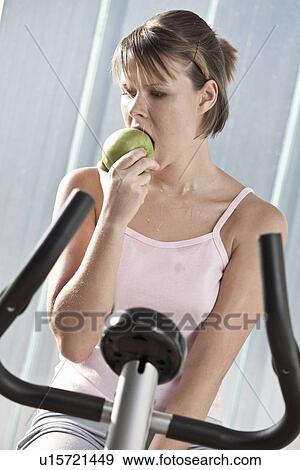 Woman eating apple on exercise machine View Large Photo Image Stock Photo - Woman eating apple on exercise machine. Fotosearch