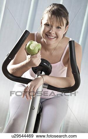 Woman eating apple on exercise machine View Large Photo Image Stock Photo - Woman eating apple on exercise machine. Fotosearch