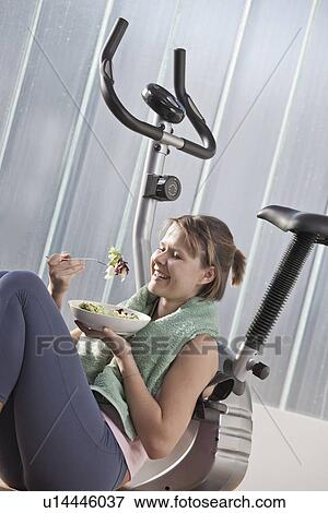 Woman eating salad by exercise machine View Large Photo Image Stock Photo - Woman eating salad by exercise machine. Fotosearch