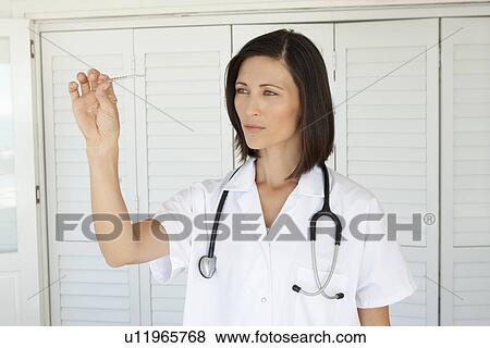 Stock Photo - Woman examining thermometer in home. Fotosearch