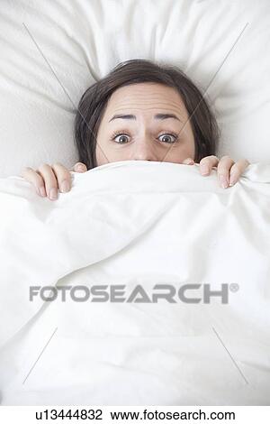 Stock Image - Woman hiding under covers in bed. Fotosearch