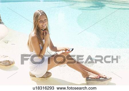 Stock Image - Woman listening to headphones by pool. Fotosearch