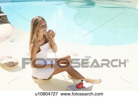 Stock Photo - Woman listening to headphones by pool. Fotosearch