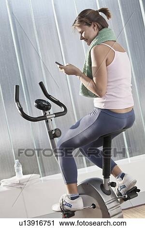 Stock Image - Woman on cell phone on exercise machine. Fotosearch