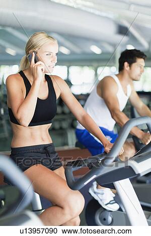 Woman on cell phone on exercise machine View Large Photo Image Stock Image - Woman on cell phone on exercise machine. Fotosearch