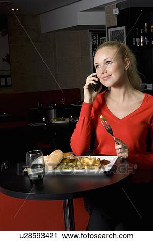 Stock Image - Woman on phone and eating in cafe. Fotosearch