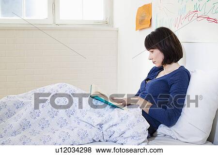 Stock Photo - Woman reading book in bed. Fotosearch