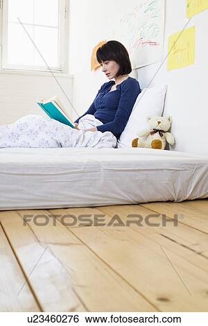 Stock Photograph - Woman reading book in bed. Fotosearch