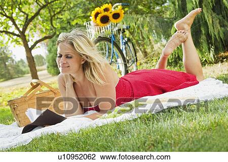 Stock Image - Woman reading book on picnic blanket. Fotosearch