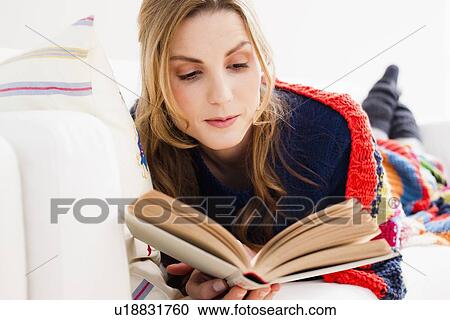 Stock Image - Woman reading book on sofa. Fotosearch