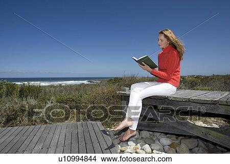 Picture - Woman reading book on wooden bench. Fotosearch