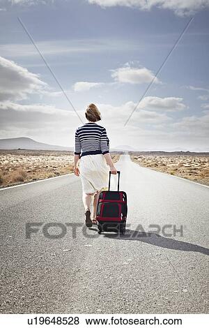 Woman rolling luggage on rural road View Large Photo Image Stock Photo - Woman rolling luggage on rural road. Fotosearch