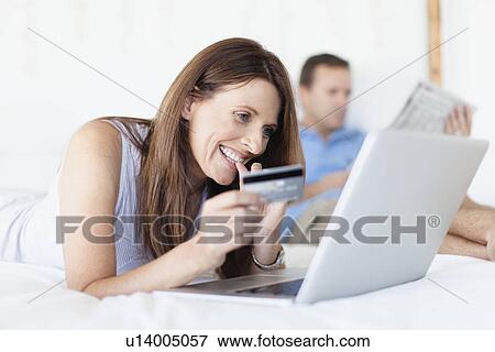 Stock Photo - Woman shopping online on bed. Fotosearch