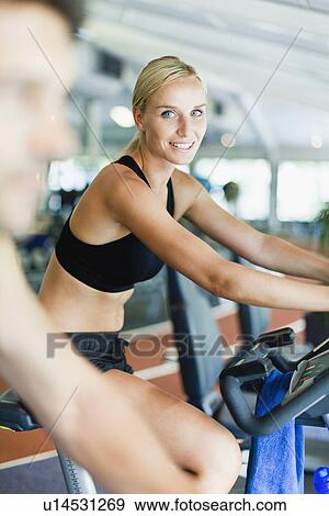Stock Photo - Woman using exercise machine in gym. Fotosearch