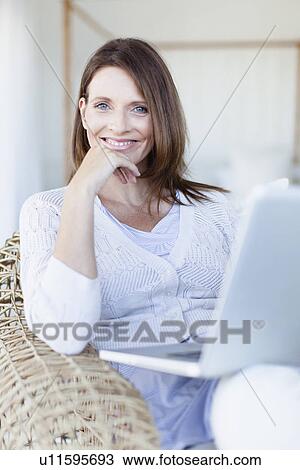 Woman using laptop in armchair View Large Photo Image Stock Image - Woman using laptop in armchair. Fotosearch