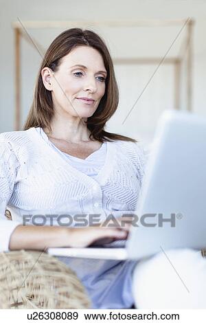 Woman using laptop in armchair View Large Photo Image Stock Photo - Woman using laptop in armchair. Fotosearch