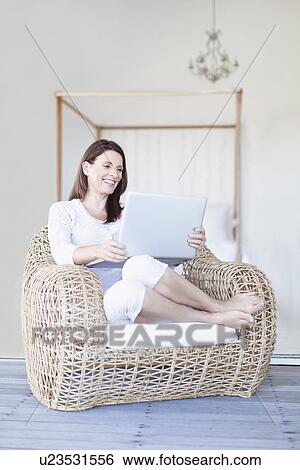 Woman using laptop in armchair View Large Photo Image Stock Photograph - Woman using laptop in armchair. Fotosearch