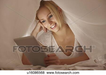 Woman using tablet computer under covers View Large Photo Image Stock Photo - Woman using tablet computer under covers. Fotosearch