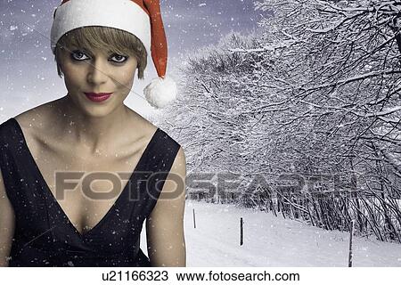 Stock Image - Woman wearing Santa hat in snow. Fotosearch