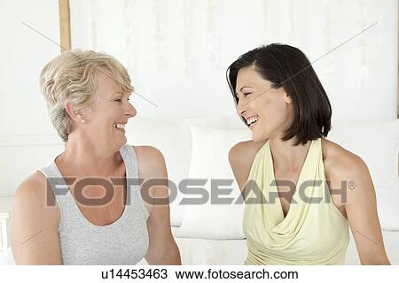 Stock Image - Women laughing together on sofa. Fotosearch
