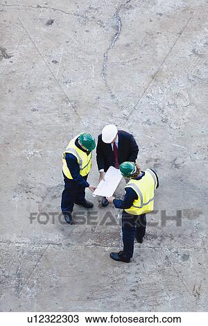 Stock Image - Workers reading blueprints at dry dock. Fotosearch